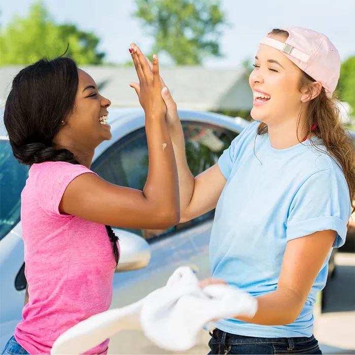 Two young women high-five as they wash cars for a local fundraiser promotion in Ontario, Canada.