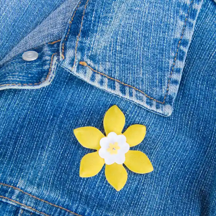 A lapel pin shaped like a flower and pinned onto a denim jacket.