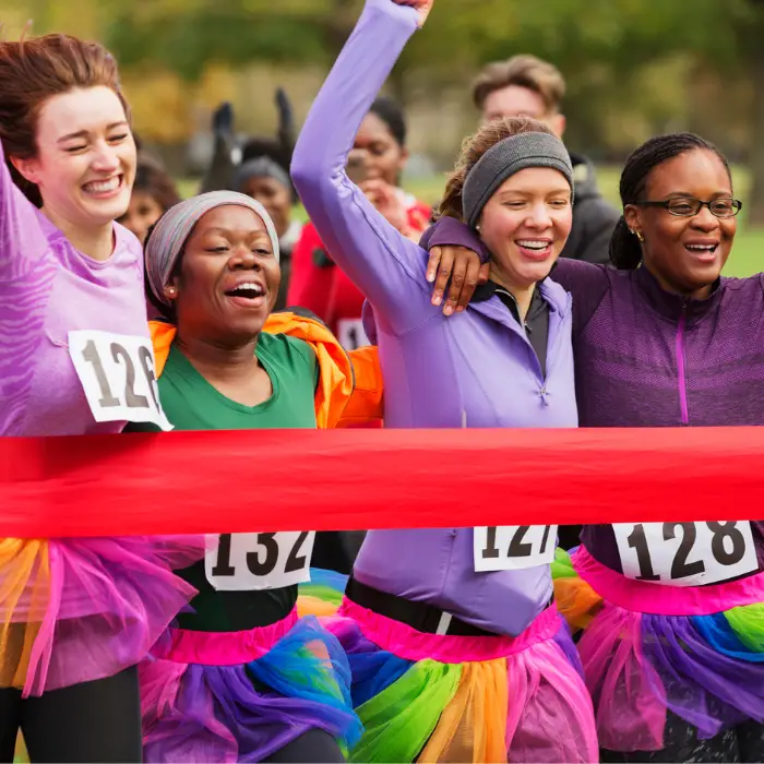 Four women cross the finish line together at a promotional fundraiser for raising awareness and support of a local charity.