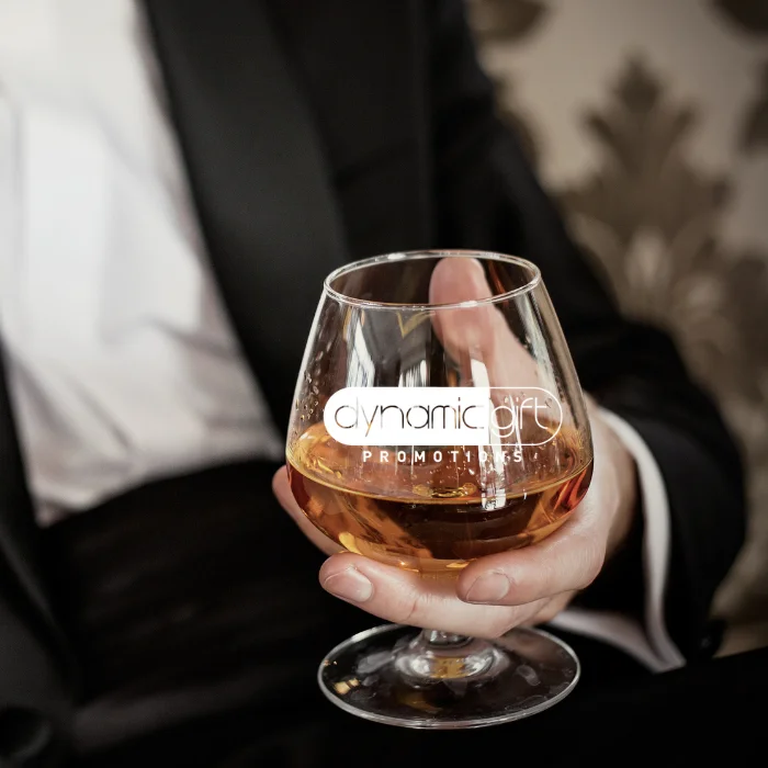 A man holding a brandy glass customized with the Dynamic Gift logo.