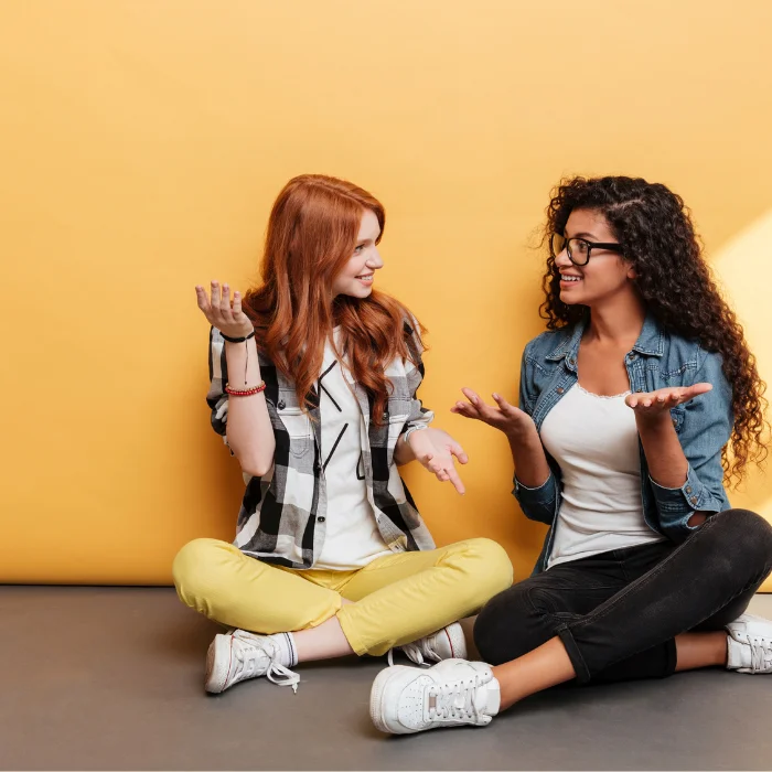 Two women sit on the floor and happily discuss their common interests.