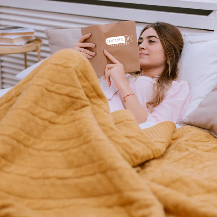 A person relaxes while reading a book at her home in Alberta snugged up with a custom blanket from Dynamic Gift.